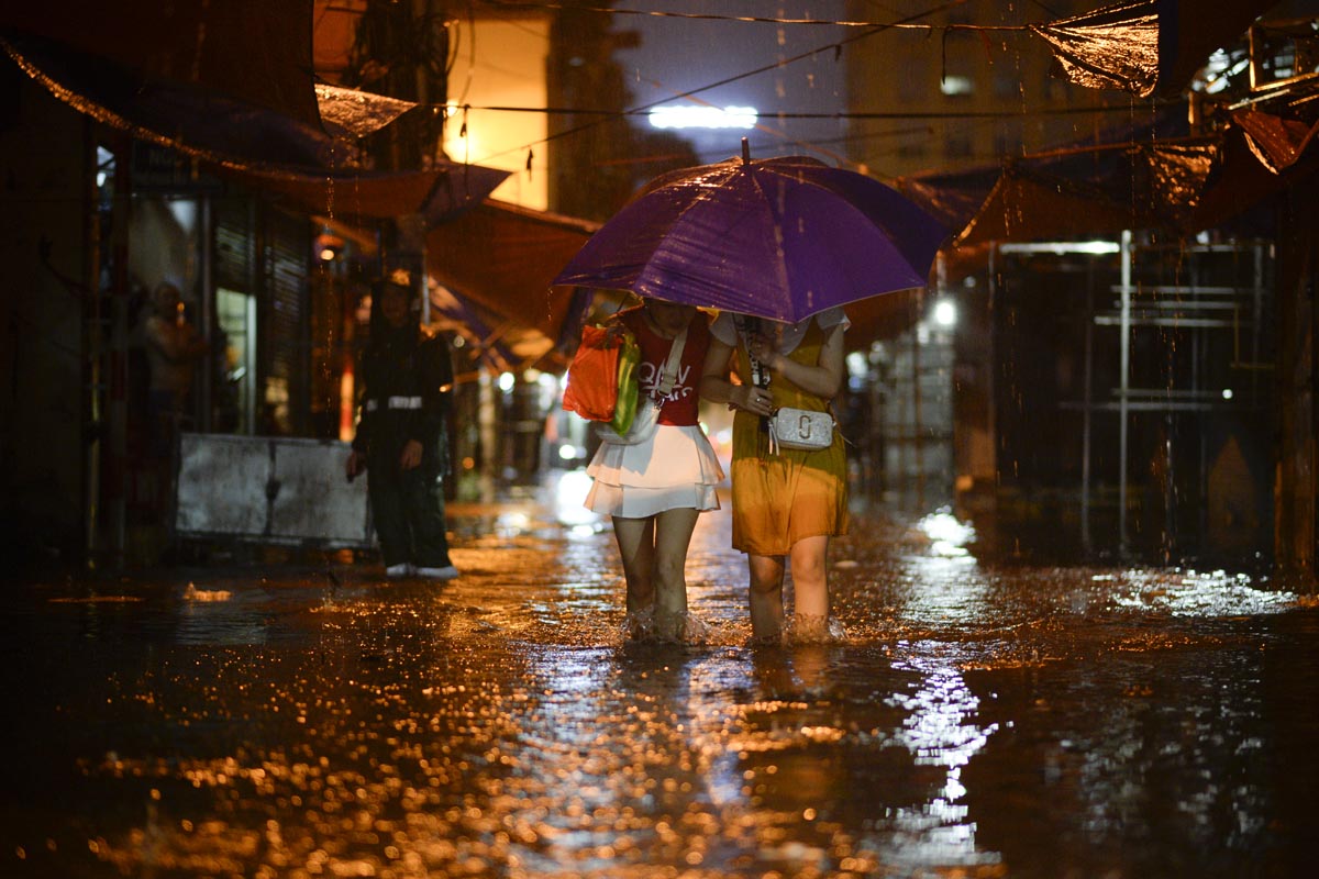 Two young women walking in flooded streets with an umbrella