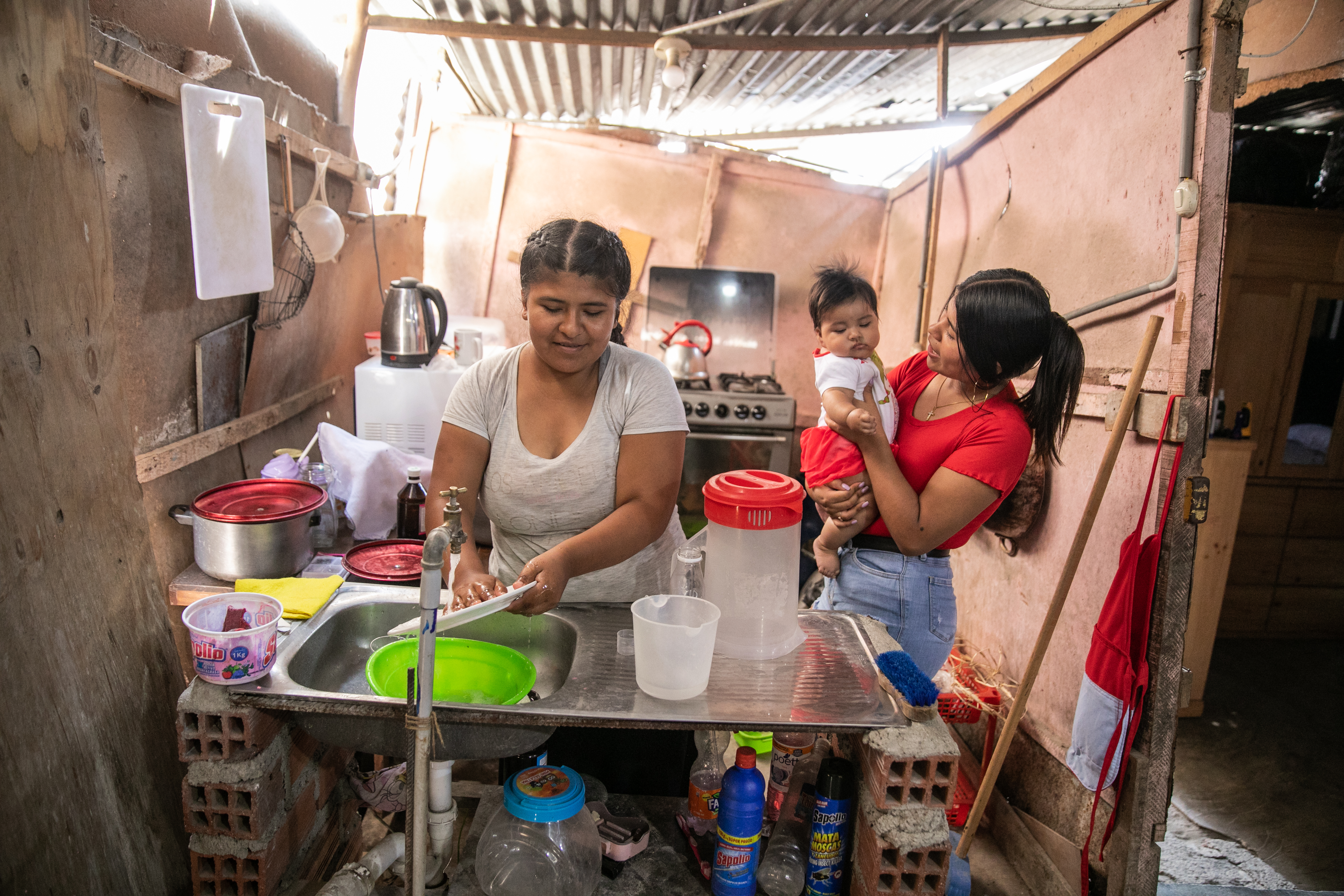 Woman washing up next to a young woman holding a baby