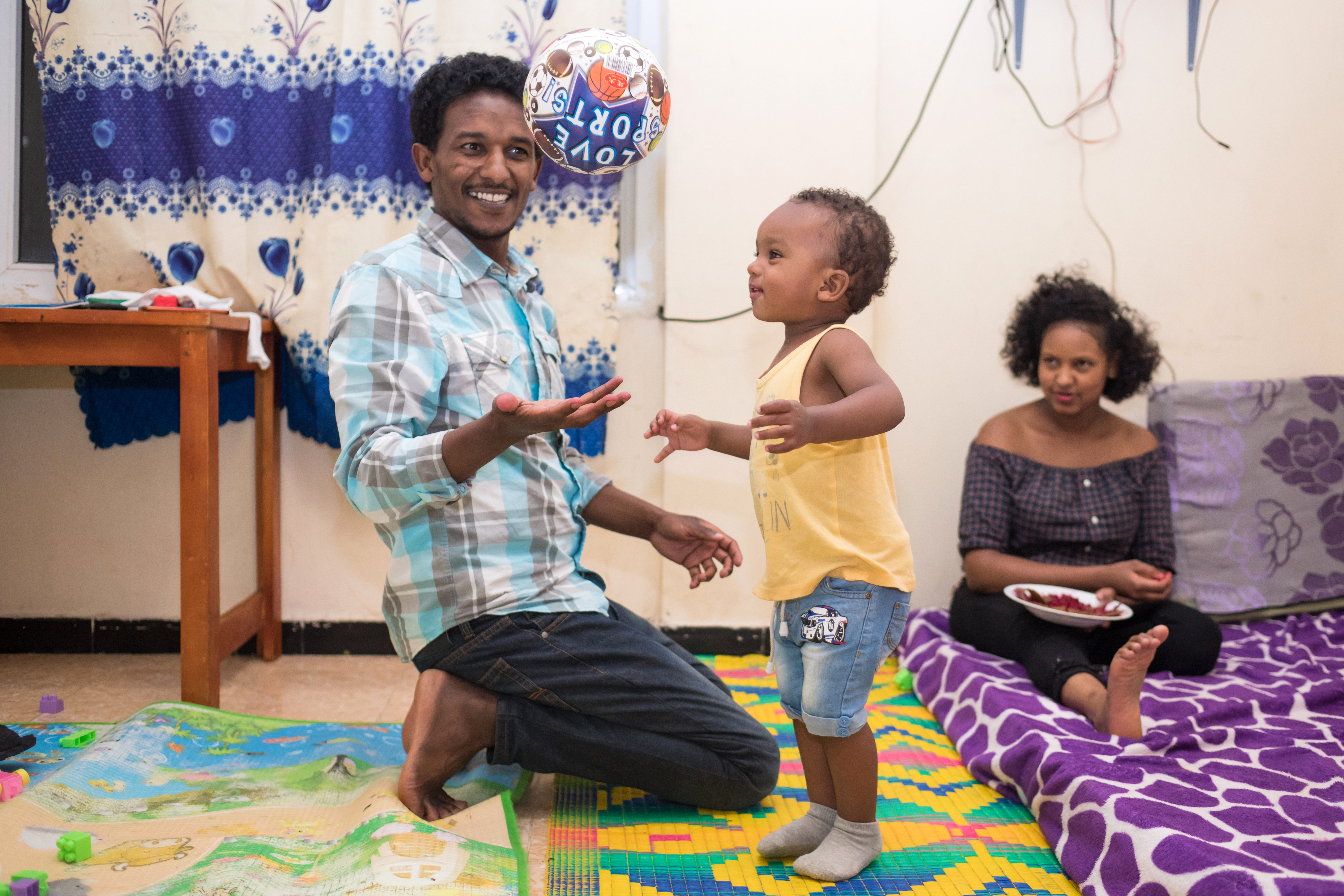 Young father playing a football with young child, and young mum sitting in background