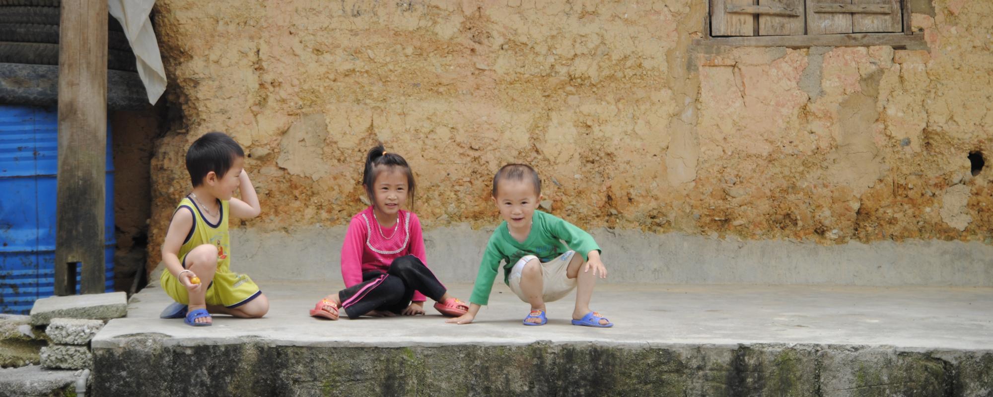 three children sitting outside a house 