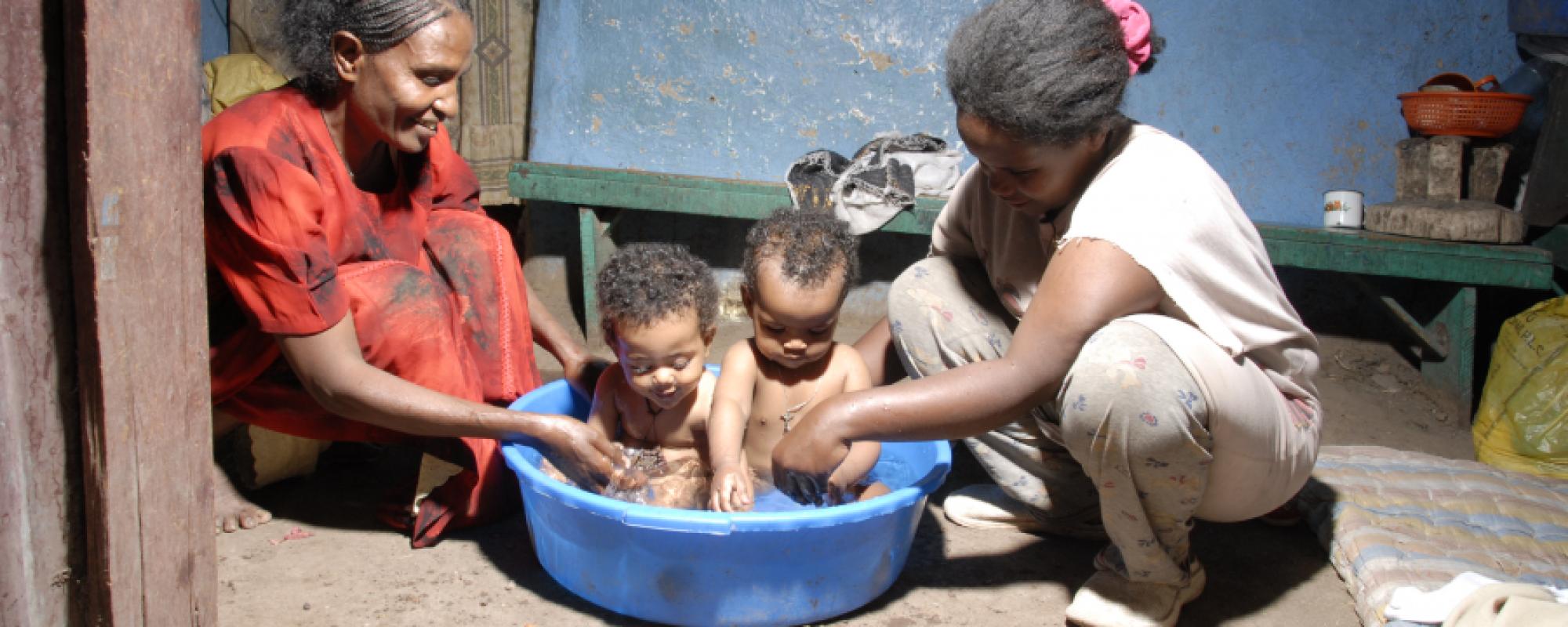 two babies having a bath in a plastic blue tub