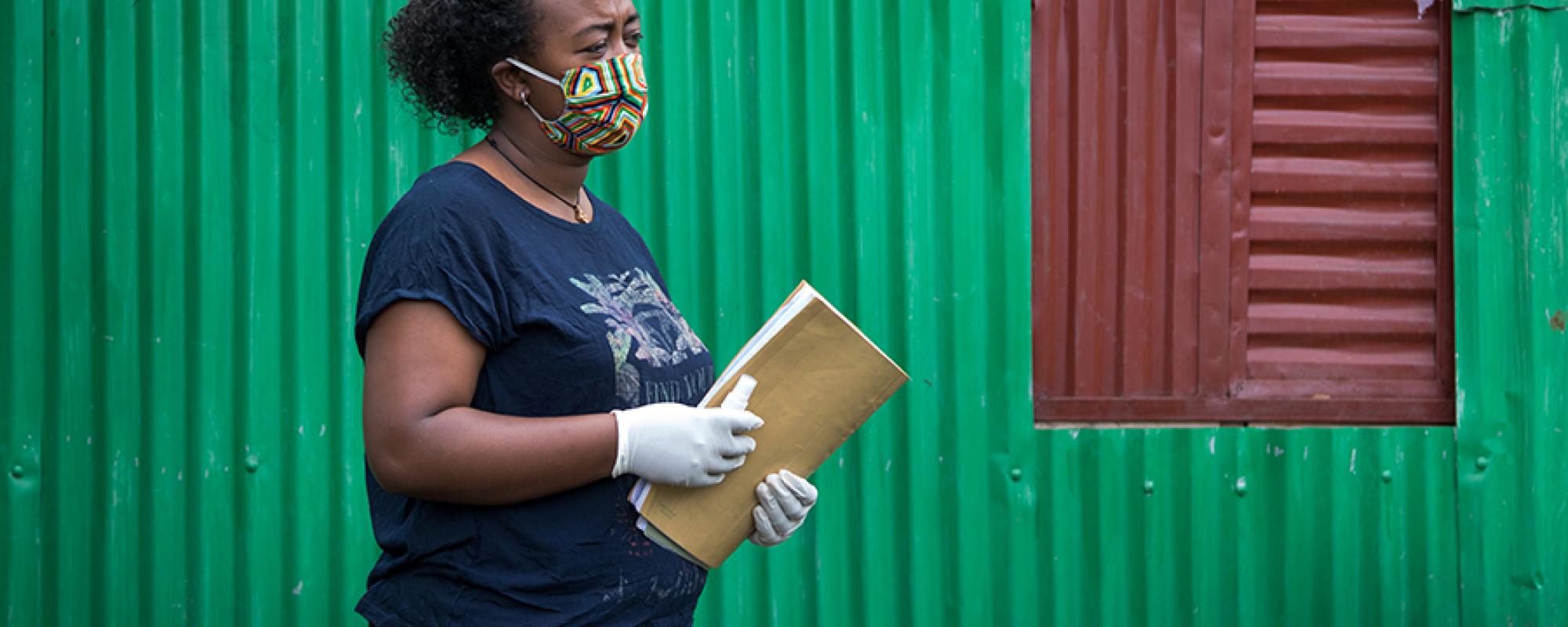 Women in mask standing by a green building
