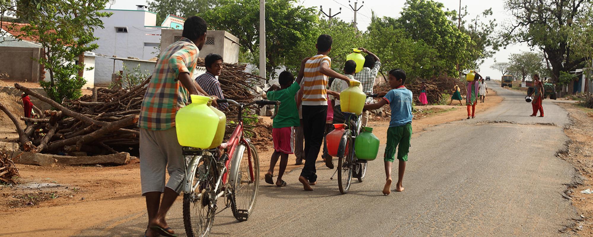 men walking down a road with bikes full of water cans