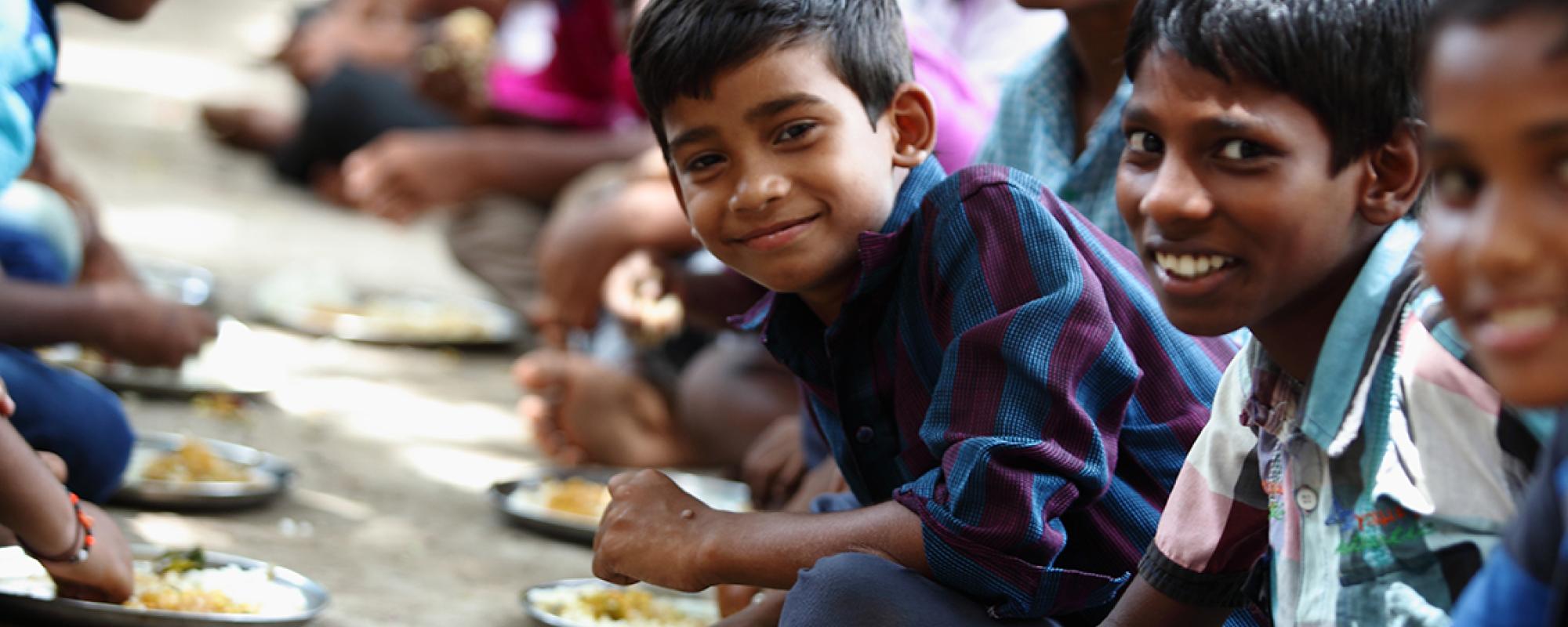 boys sitting in a line on the floor eating