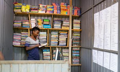 Young man reading a book, stood in front of book shelves in a shop