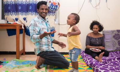 Young father playing a football with young child, and young mum sitting in background