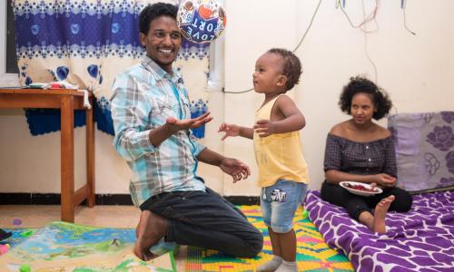 Young father playing a football with young child, and young mum sitting in background