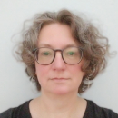 Helen Andrews looking directly into the camera, a grey background behind her